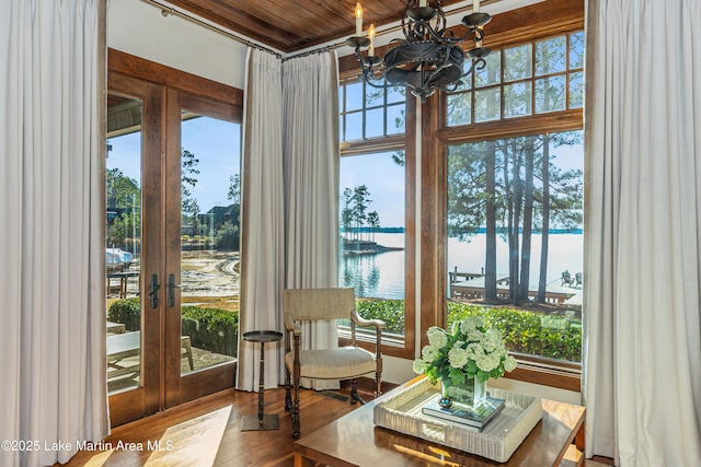 sunroom with a notable chandelier, a wealth of natural light, french doors, and a water view