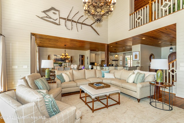 living room featuring an inviting chandelier, light hardwood / wood-style floors, a high ceiling, and wood walls