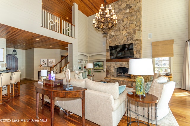 living room with hardwood / wood-style flooring, an inviting chandelier, a towering ceiling, a stone fireplace, and wooden ceiling