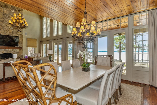 dining area with an inviting chandelier, a water view, dark hardwood / wood-style flooring, a stone fireplace, and french doors