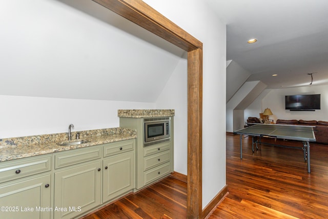 kitchen featuring vaulted ceiling, stainless steel microwave, sink, light stone countertops, and dark wood-type flooring