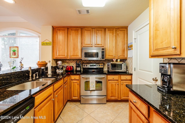 kitchen featuring ornamental molding, stainless steel appliances, sink, light tile patterned floors, and dark stone countertops