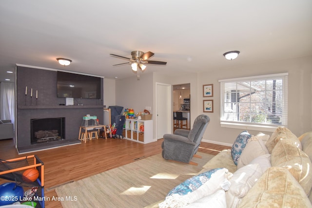 living room with ceiling fan, wood-type flooring, and a brick fireplace