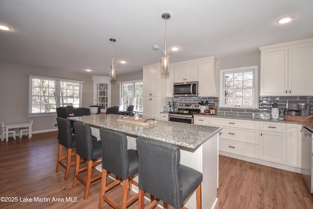 kitchen with pendant lighting, a center island, white cabinets, light stone countertops, and stainless steel appliances