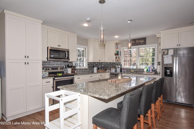 kitchen featuring white cabinetry, a center island, hanging light fixtures, light stone counters, and appliances with stainless steel finishes