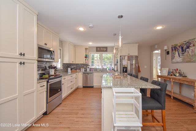 kitchen with light stone countertops, appliances with stainless steel finishes, decorative backsplash, a center island, and hanging light fixtures