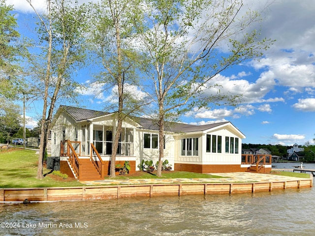 back of property with a sunroom, a yard, a water view, and central AC unit