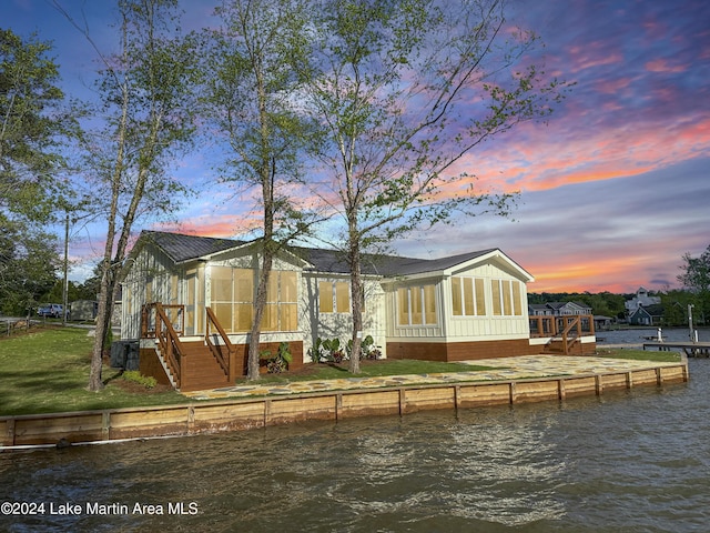 back house at dusk with a yard, a water view, and central air condition unit