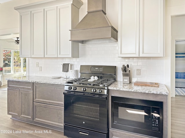 kitchen featuring ceiling fan, light stone countertops, light hardwood / wood-style flooring, premium range hood, and black appliances