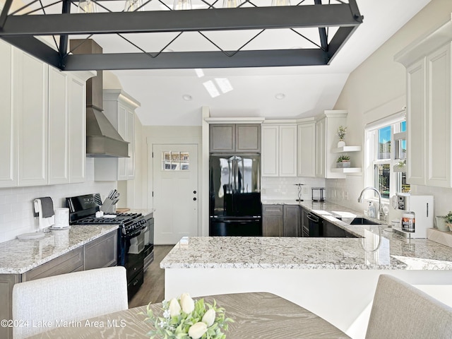 kitchen featuring a breakfast bar, black appliances, sink, wall chimney exhaust hood, and tasteful backsplash