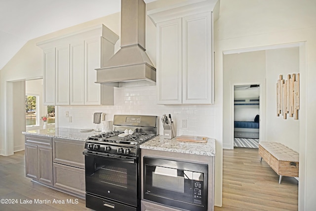 kitchen featuring light stone countertops, white cabinetry, custom exhaust hood, black appliances, and light wood-type flooring