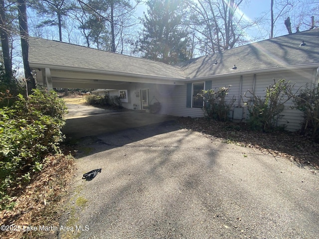 view of side of home featuring driveway, a shingled roof, and an attached carport