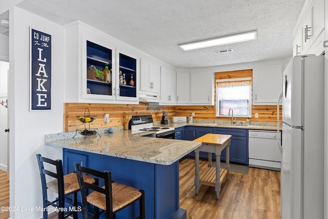 kitchen featuring white appliances, blue cabinets, sink, a kitchen bar, and kitchen peninsula