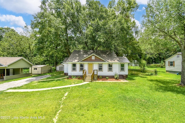1706 Simpson St, Alexander City, AL 35010 - bungalow with a storage unit, driveway, a front lawn, and view of wooded area
