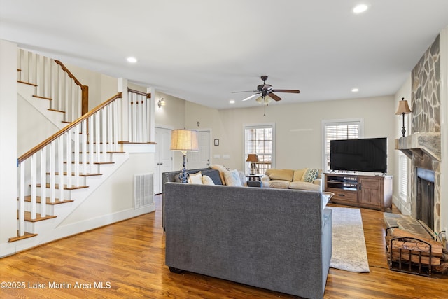 living room featuring visible vents, stairway, wood finished floors, a stone fireplace, and recessed lighting