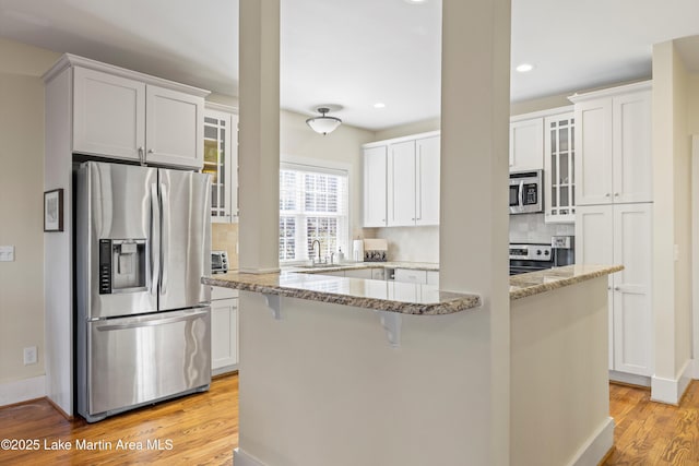 kitchen with light wood-style flooring, glass insert cabinets, appliances with stainless steel finishes, a sink, and backsplash