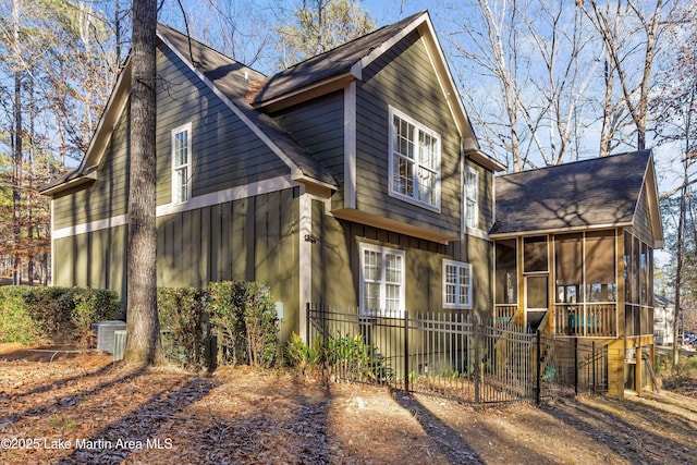 view of home's exterior with a shingled roof, a sunroom, fence, central AC, and board and batten siding