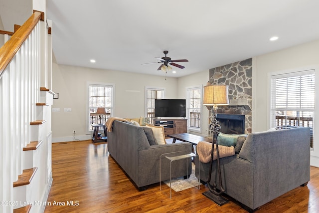 living area featuring stairs, a fireplace, a ceiling fan, and wood finished floors