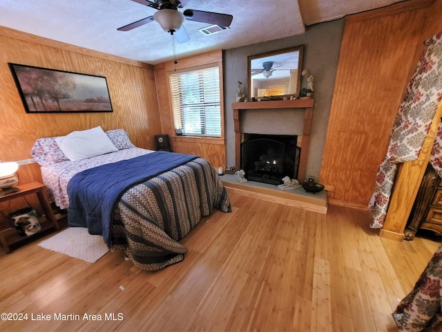 bedroom featuring a textured ceiling, light hardwood / wood-style floors, ceiling fan, and wooden walls