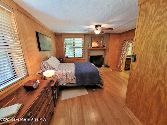 bedroom featuring ceiling fan, light hardwood / wood-style flooring, a textured ceiling, and wooden walls