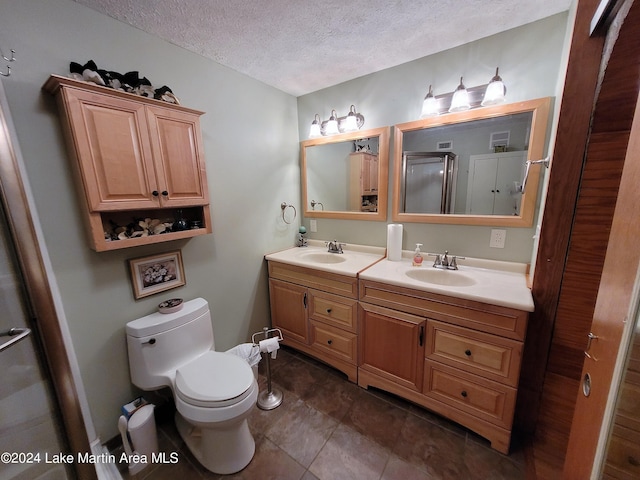 bathroom featuring vanity, tile patterned flooring, toilet, a textured ceiling, and a shower with shower door