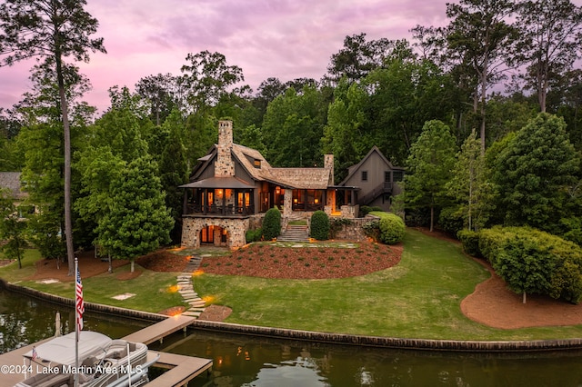 back house at dusk with a water view and a lawn