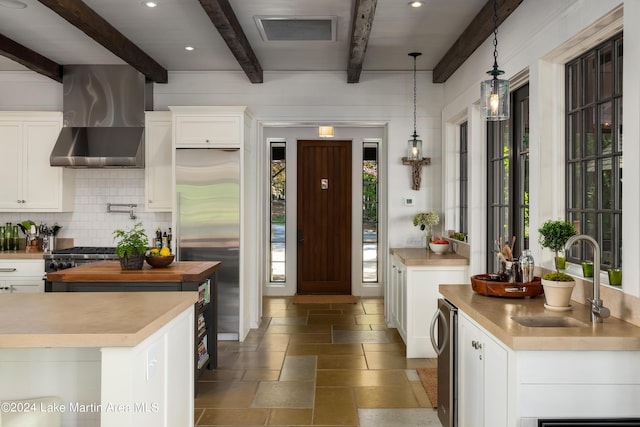 kitchen featuring beamed ceiling, premium appliances, wall chimney exhaust hood, and plenty of natural light