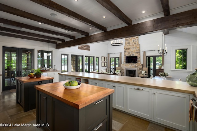 kitchen with french doors, white cabinets, a fireplace, beamed ceiling, and a kitchen island