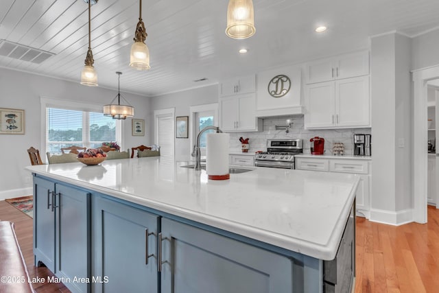 kitchen with gas range, decorative light fixtures, an island with sink, and white cabinets