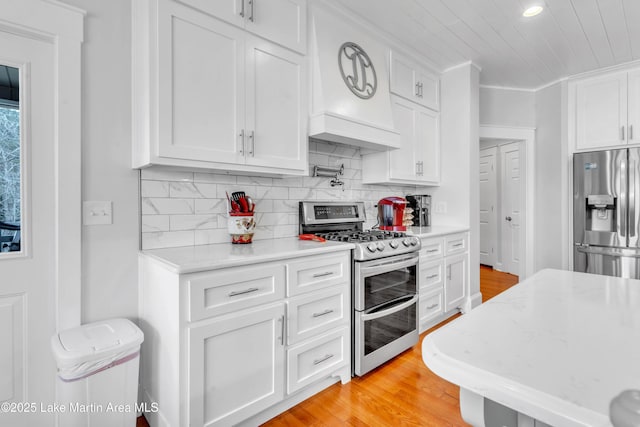 kitchen with stainless steel appliances, white cabinetry, light wood-type flooring, and decorative backsplash