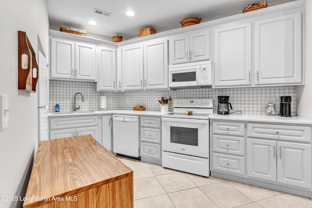 kitchen with light tile patterned flooring, sink, backsplash, white cabinets, and white appliances