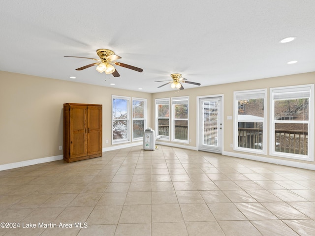 unfurnished living room with ceiling fan, light tile patterned flooring, a textured ceiling, and a wealth of natural light