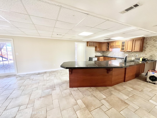 kitchen featuring kitchen peninsula, a paneled ceiling, backsplash, and a breakfast bar area