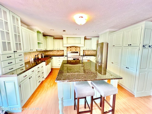 kitchen with light wood-type flooring, a textured ceiling, white range with electric stovetop, stainless steel refrigerator, and an island with sink