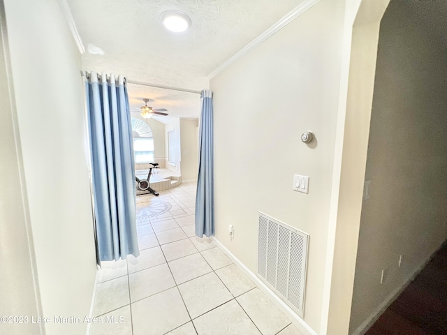 hallway with a textured ceiling, light tile patterned floors, and crown molding