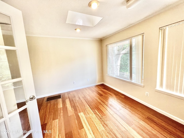 spare room with hardwood / wood-style flooring, a textured ceiling, crown molding, and a skylight