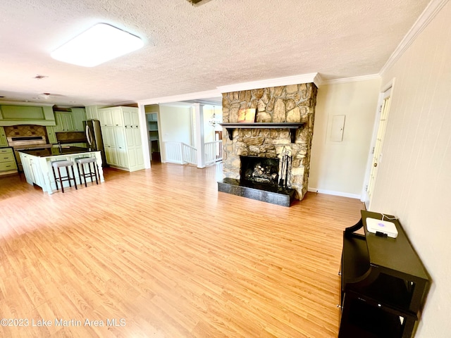 living room featuring a textured ceiling, light wood-type flooring, a fireplace, and ornamental molding