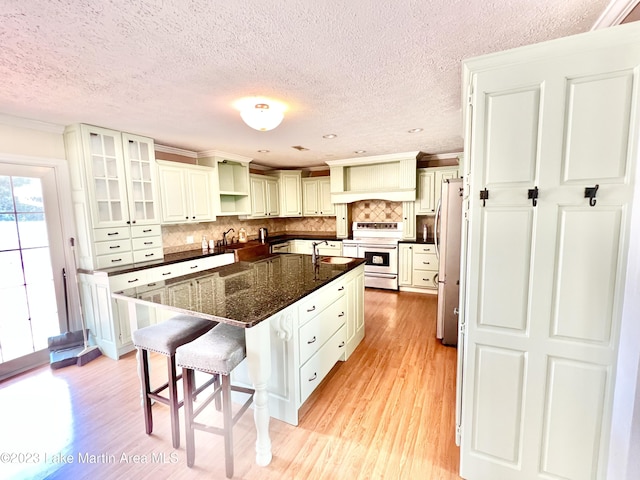 kitchen featuring a kitchen breakfast bar, backsplash, stainless steel fridge, electric stove, and a kitchen island