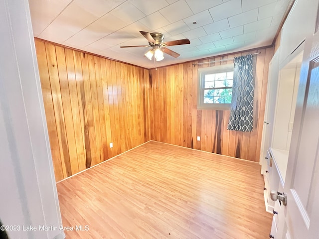 empty room featuring ceiling fan, wood walls, and wood-type flooring