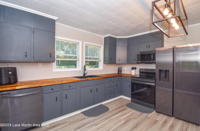 kitchen featuring pendant lighting, wooden counters, crown molding, sink, and stainless steel appliances