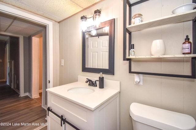 bathroom with vanity, wood walls, a drop ceiling, toilet, and wood-type flooring