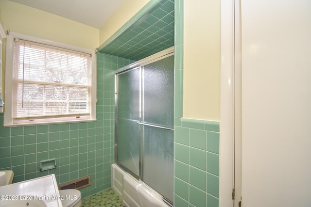 bathroom with toilet, enclosed tub / shower combo, and tile walls