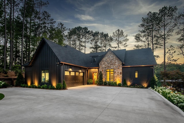 view of front facade with board and batten siding, driveway, a garage, a shingled roof, and stone siding