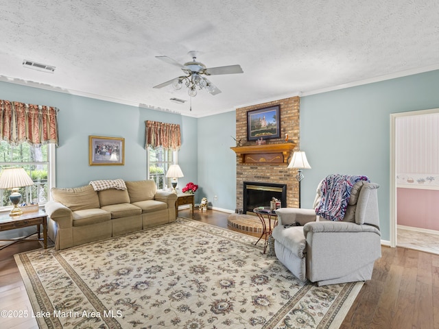 living area featuring wood finished floors, a ceiling fan, a brick fireplace, a textured ceiling, and visible vents