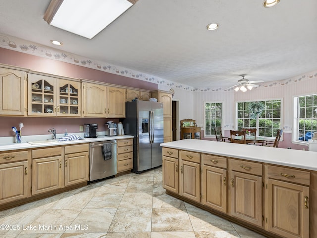 kitchen featuring glass insert cabinets, a ceiling fan, a sink, stainless steel appliances, and light countertops