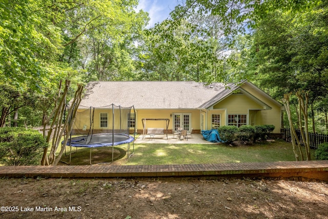 back of house with fence, a trampoline, french doors, a patio, and a lawn