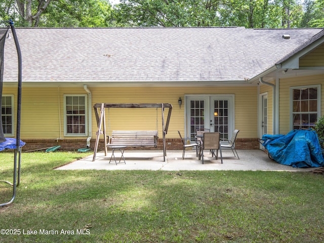 rear view of house featuring a shingled roof, a trampoline, a patio, and a lawn