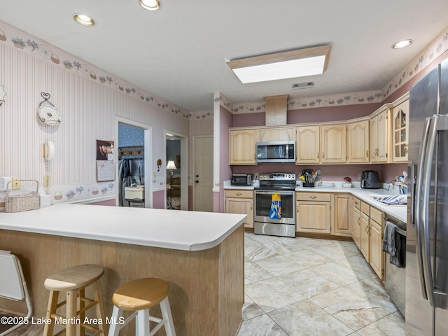 kitchen featuring light brown cabinetry, a breakfast bar, visible vents, a peninsula, and appliances with stainless steel finishes