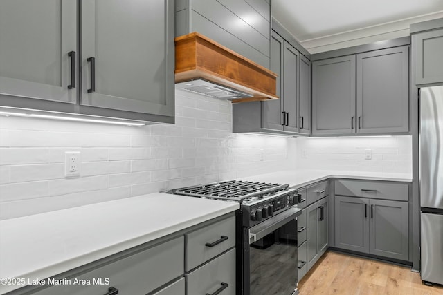 kitchen featuring gray cabinetry, premium range hood, light countertops, freestanding refrigerator, and gas stove