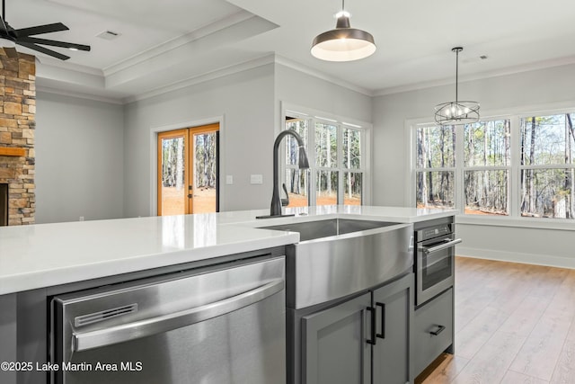 kitchen with stainless steel appliances, a sink, light wood-style floors, light countertops, and ornamental molding